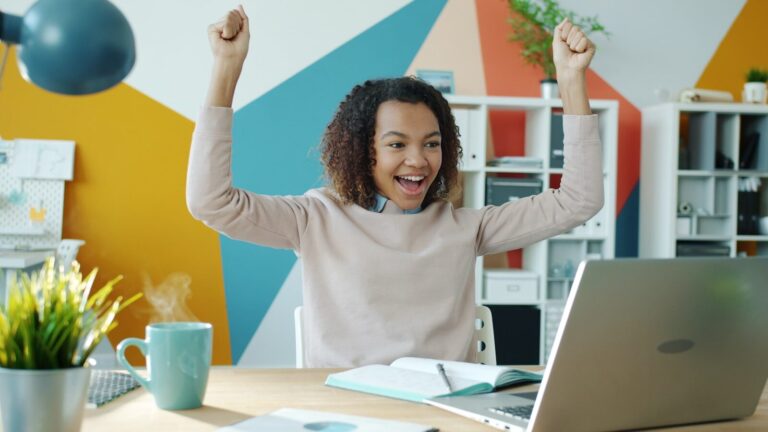 Young woman celebrating success at her desk.